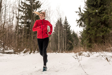 Young beautiful running woman in snowy winter forest trail. RUN