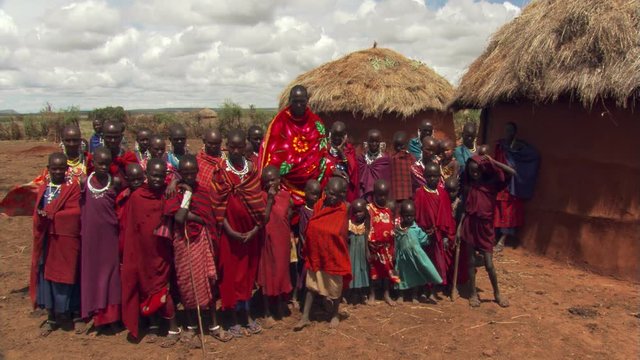 Masai villagers posing for group portrait near thatched huts on East African plain