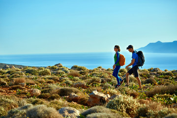 couple of travelers with backpack walking on the trail against sea and blue sky at early morning. Balos beach on background, Crete, Greece - obrazy, fototapety, plakaty