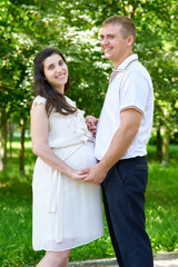 Obraz premium pregnant woman with husband posing in the city park, family portrait, summer season, green grass and trees