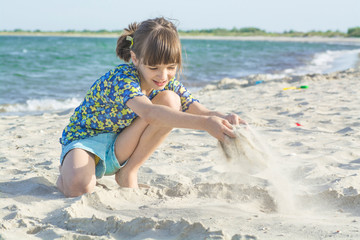 Girl on the shore playing with sand on a background of sea and waves