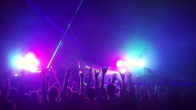 Crowd partying, dancing slow motion at a concert. The crowd raises his hands up and dancing