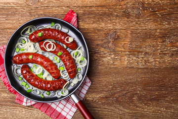 Fried sausages in a pan with onions.