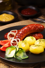Grilled sausages in a pan with onions, served with boiled potato