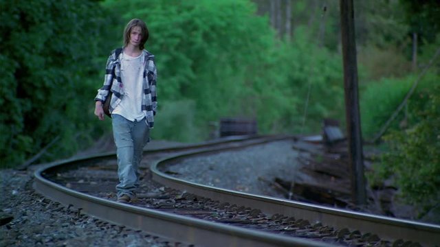 Thin, ragged, teenage boy walking along curving railroad tracks
