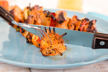 Fleischspieße auf blauem Teller. Fleisch wird mit Besteck geschnitten. Spiegelung im Messer.