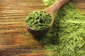 Wooden spoon with powdered matcha green tea on wooden table