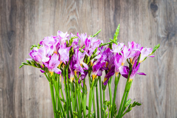 Freesia flowers in the vase on wooden background