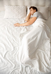 Fototapeta na wymiar Young man sleeping alone in white big bed