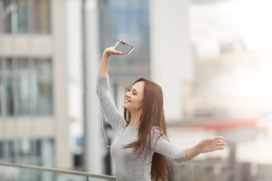 Beautiful young woman holding a phone with headphones and dancing with eyes closed.