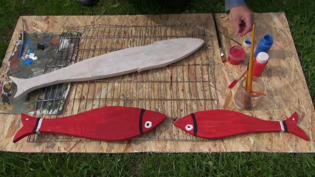 Man decorating wooden fish with acrylic red and white paint

