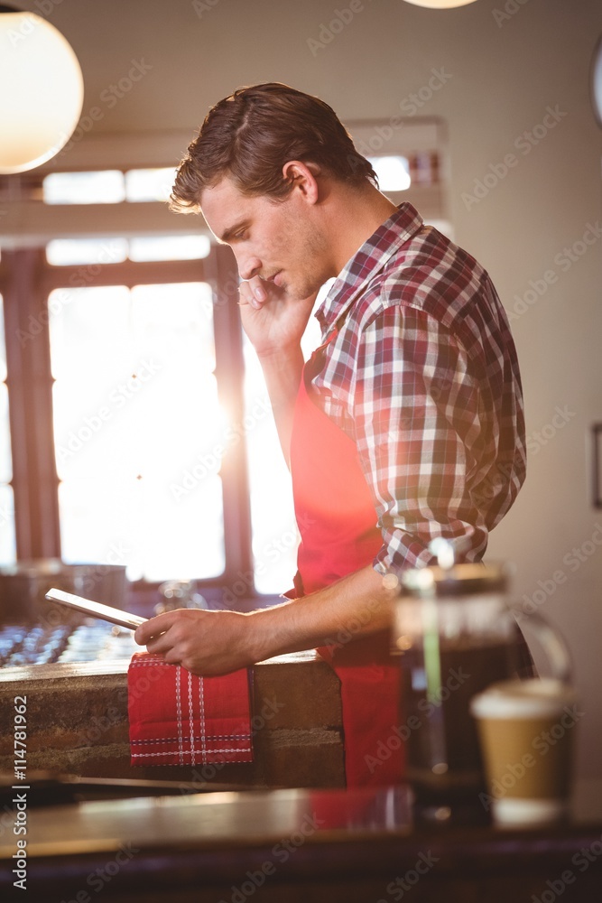 Poster waiter talking on mobile phone while using digital tablet