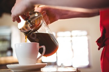 Mid section of waiter pouring a cup of coffee
