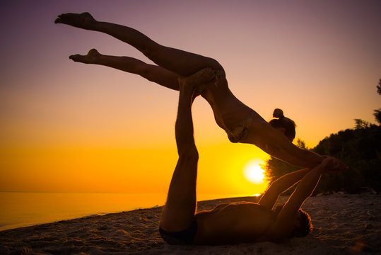 An attractive young woman and man doing yoga on the beach, Sea