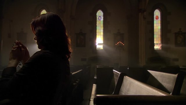 Woman in dimly lit church saying prayers with rosary