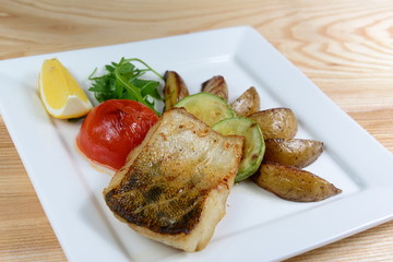 Grilled fish with vegetables on a white square plate, close-up