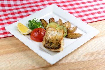 Grilled fish with vegetables on a white square plate, foreground 