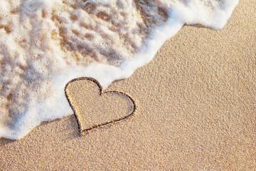 heart symbol handwritten on sandy beach with soft ocean wave