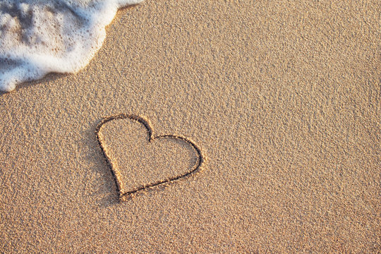 heart symbol handwritten on sandy beach with soft ocean wave