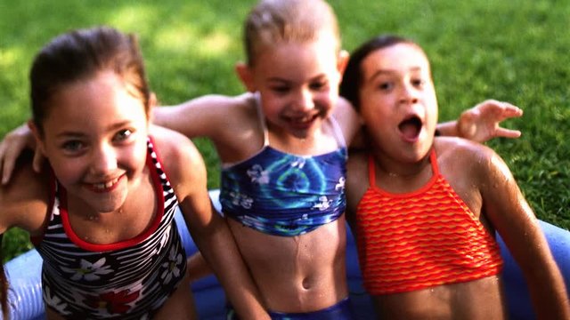 Three girls standing arm in arm before falling backward into a swimming pool