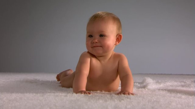 Smiling baby in diaper on white rug, trying to crawl