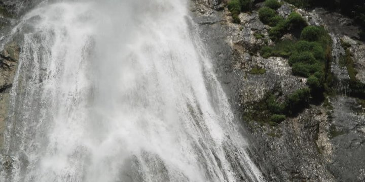 Tilt-down on a leaping waterfall veiling a rocky cliff face