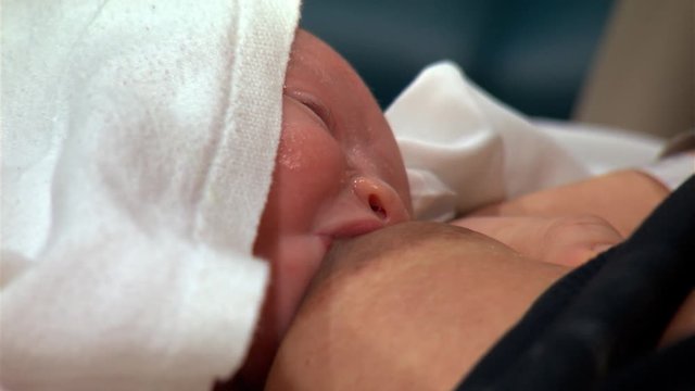 Close-up face of newborn baby sucking at mother's nipple
