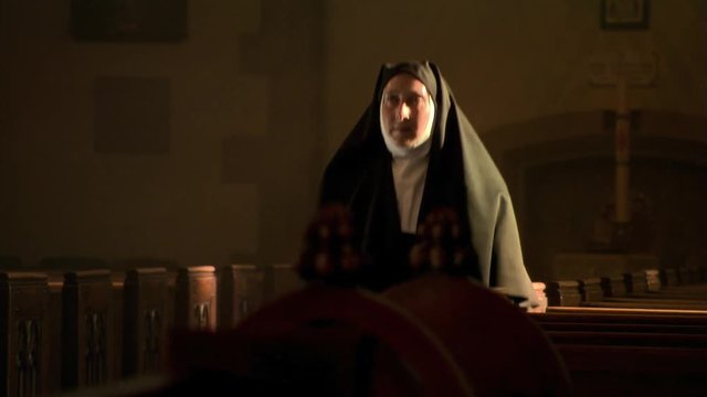 Kneeling nun rising from solitary prayers and leaving nave of church