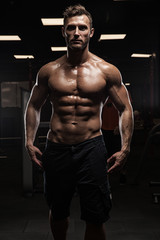 Naklejka na ściany i meble Muscular bodybuilder guy doing exercises with dumbbells in gym