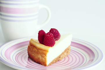 cheesecake with two raspberries on top of the saucer on a light background. Photo in high-key. Cup blurred in the background
