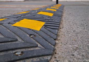 Bolted down speed bump made of rubber on asphalt road, closeup
