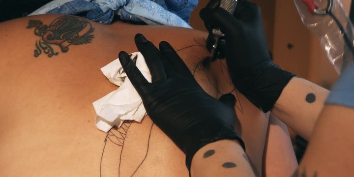 Hands of a tattoo artist inking a design on a customer's back