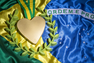 Large heart shaped gold medal surrounded by laurel wreath resting on shiny Brazil flag background...