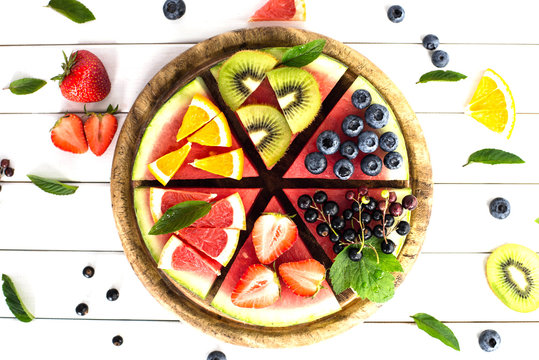 Sliced juicy watermelon pizza on white wooden table.  Watermelon, blueberries, grapefruit, orange,kiwi,strawberry,black currant,mint.Concept for healthy Eating. Eye bird view.