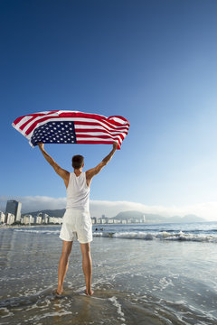 Athlete in white outfit standing with American flag waving in the wind on the shore of Copacabana Beach, Rio de Janeiro, Brazil