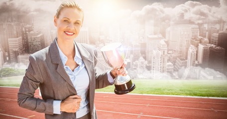 Composite image of successful businesswoman holding a trophy