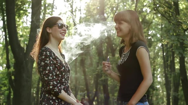 Girls talking sweet stories and smoking the e-cigarette in the park
