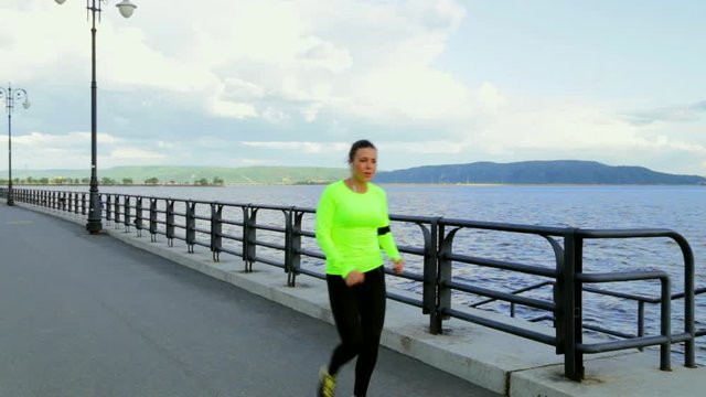 Caucasian brunette woman in sports cloth runs on embankment near the river full HD
