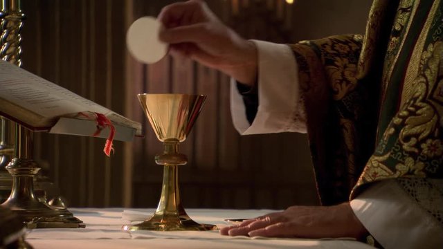 Hands of priest with wafer and chalice during Eucharist