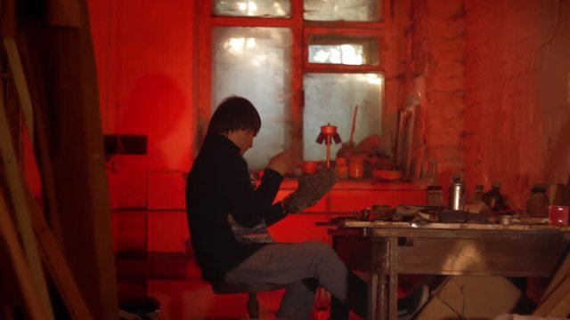 The artist paints a mask in a dark studio with a red light
