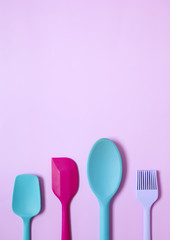 Colourful silicone baking utensils on a pink background forming a cooking themed a page border