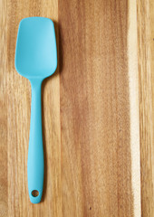 A blue silicone baking spatula on a wooden background forming a page border