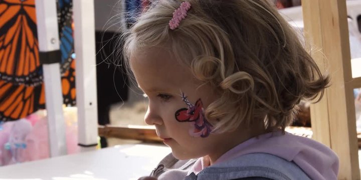 Little girl having her face painted at a carnival