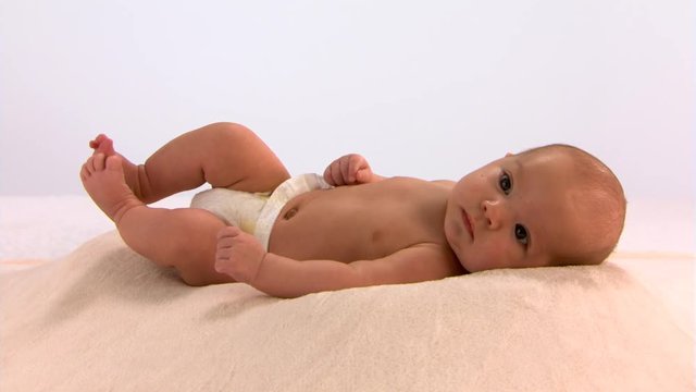 Baby in diaper lying on pillow, kicking and squirming contentedly