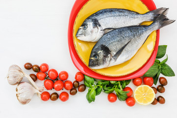 Two fresh dorado fish on plate and vegetables on the white table. Top view, copy space. 