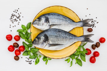 Raw fish on yellow plate. Dorada with basil and tomatoes. Top view, copy space