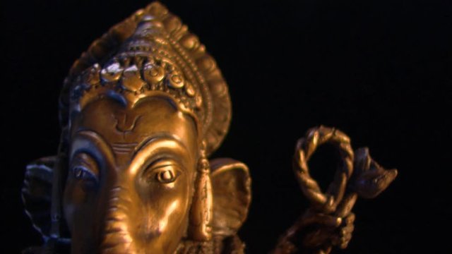 Golden statue of Ganesha revealed against a black frame