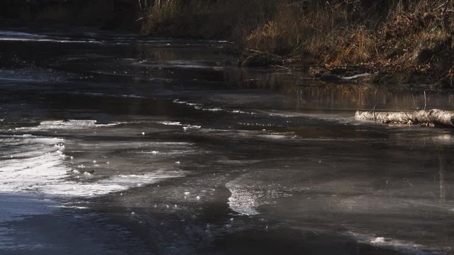 A narrow current flowing through a thin layer of ice on a forest stream