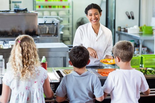 Cheerful woman serving food to schoolchildren 