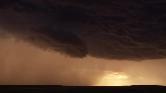 Dramatic lightning flash at edge of a bronze-colored cloud pouring rain on a dark landscape, time lapse